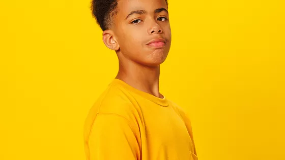 photograph of young man, wearing a yellow t-shirt against a yellow background, looking straight at camera determinedly  