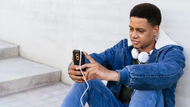 A young person concentrating on his mobile phone with headphones around his neck.