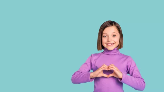 A little girl in a purple t-shirt making a heart with her hands in front of her chest