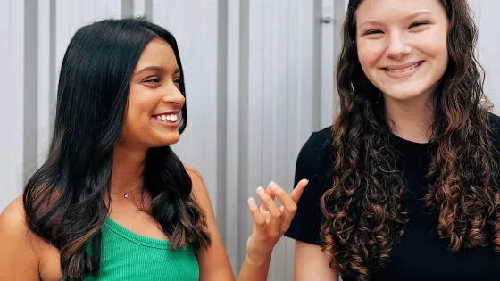 Photograph of two young woman laughing, one facing camera one facing her friend