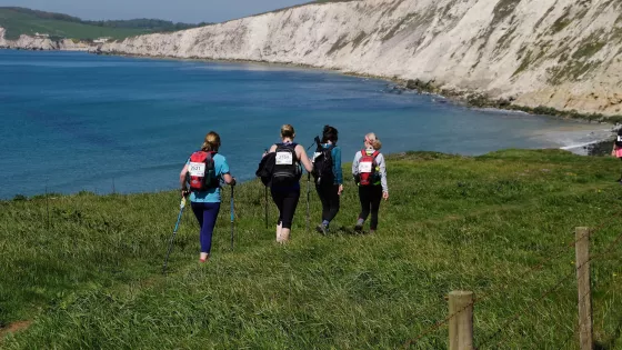 4 women walking along a cliff path with views of the sea