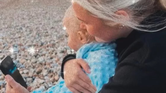 A mother holds her son sitting on a beach