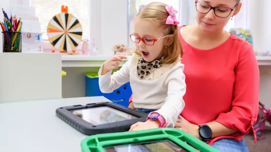 Child playing happily with tablet, sat on a carers knee