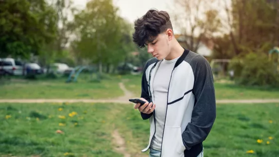 Young boy looks solemnly at his phone outside.