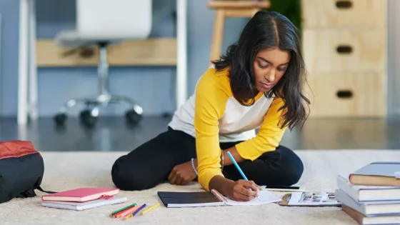 A teenager, sat on the floor, writes notes down in a diary.