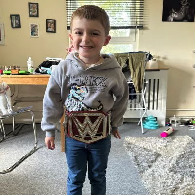 A young boy stands posing with a wrestler's belt.