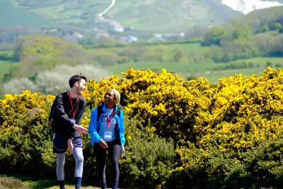 A man and women chatting and walking in front of yellow bushes 