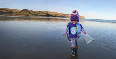 A cute child wearing a Young Epilepsy Purple Day t-shirt walks on the beach with a hat covering face.