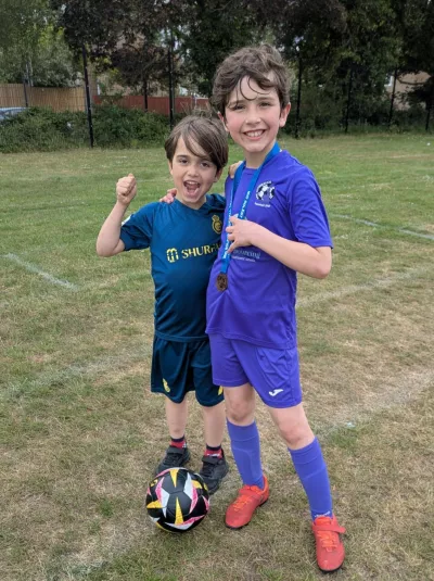 Two boys in football gear celebrate a medal in a football field.