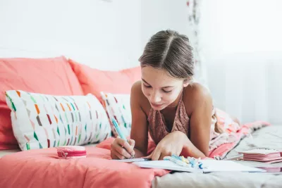 A girl writes in her diary on her bed.
