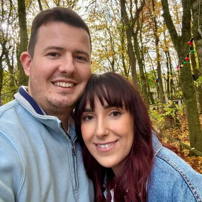 A young couple in denim smile in a woodland.
