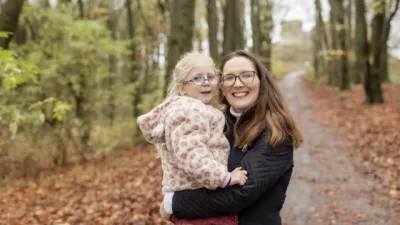 A mother and daughter smile in a forest.