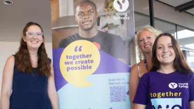 Three women stand around a Young Epilepsy poster.