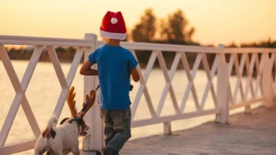 A young boy and dog walk wearing Christmas hats.