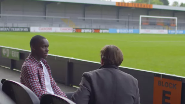 Renell talking to his support worker by a football pitch