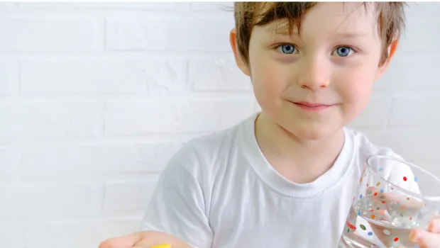 A young boy holds a glass and medication.