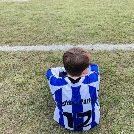 Boy in blue and white football kit sitting next to a football pitch