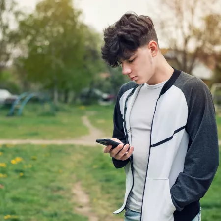 Young boy looks solemnly at his phone outside