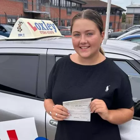 A young woman stands by a learner car, showing that she passed her driver's license.