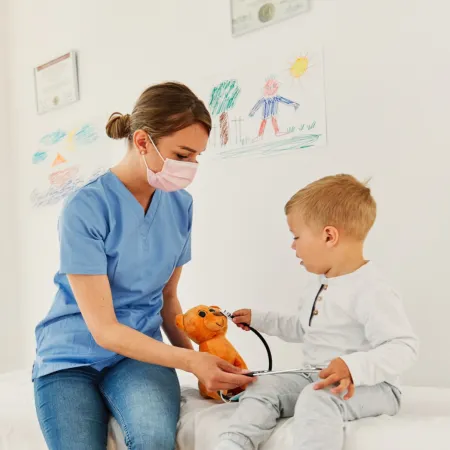 A nurse plays with a young patient and teddy bear.