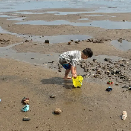 A young boy plays with a bucket on a beach.