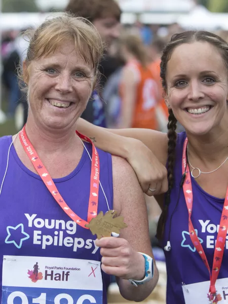 Two women in Young Epilepsy running vests, smiling at the camera proudly showing their medals.