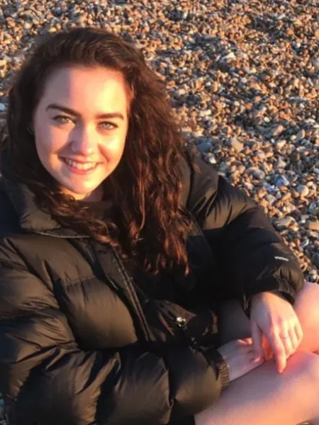 photograpgh of young woman on a pebble beach, smiling at the camera with the evening sun on her face 