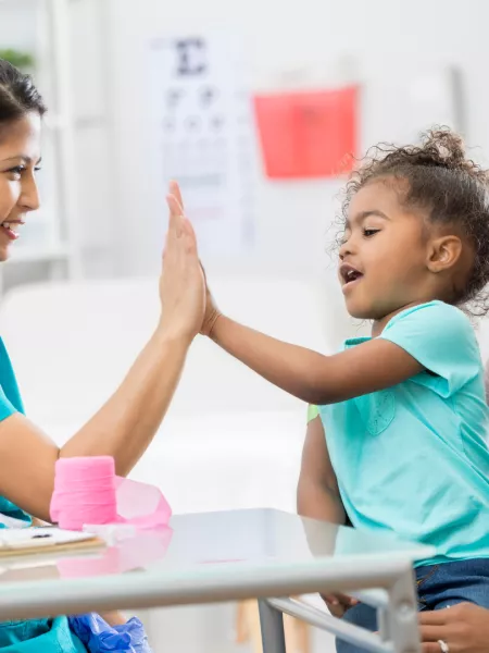 Nurse giving a child a high five whilst she sits on her mums lap