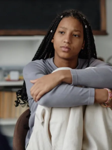 A teenage girl looks serious, with her arms wrapped around her knees.