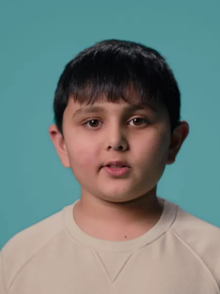 A young Asian boy stands against a blue backdrop wearing a white t-shirt