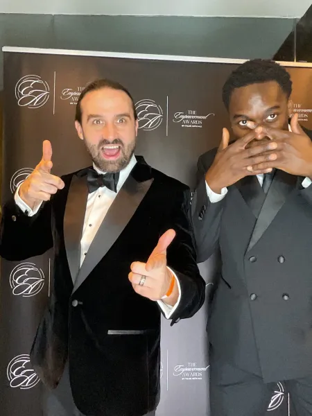 Two young men in suits stand at the step-and-repeat at the Empowerment Awards.