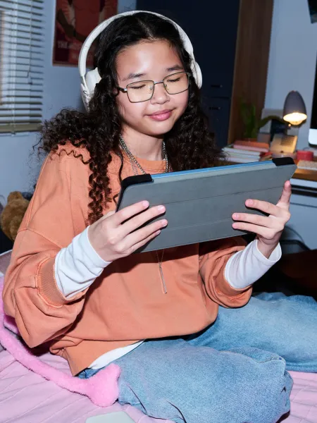 A teenage girl uses a tablet while wearing headphones.